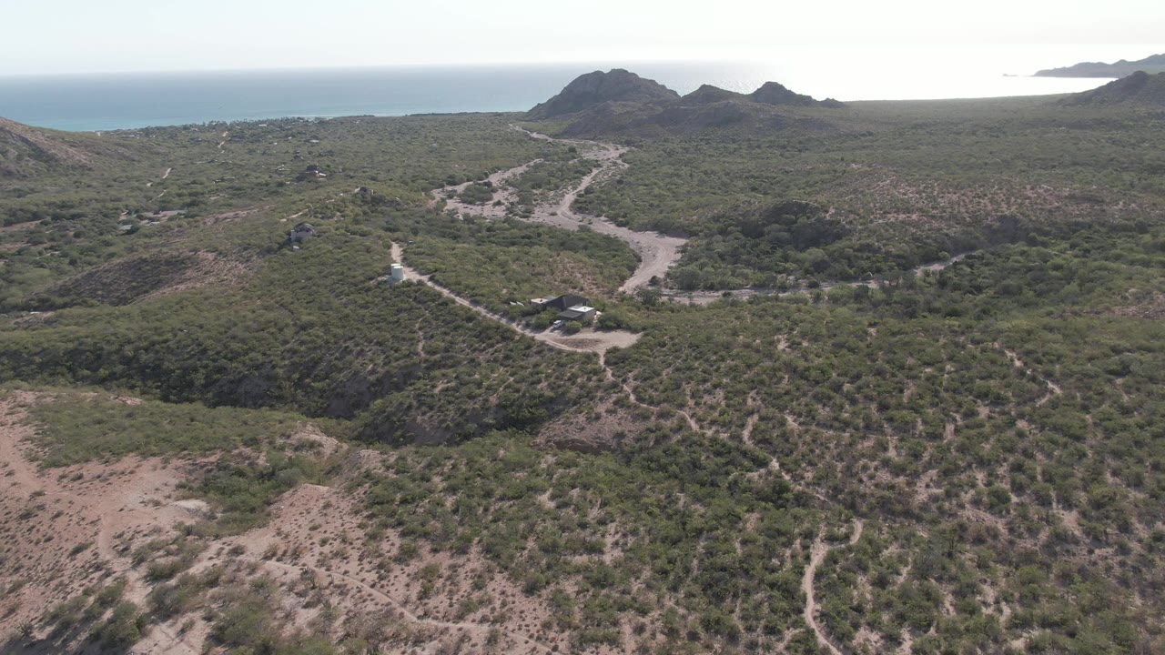 Aerial view of a white vehicle on a winding dirt road through scrubby hills near the ocean.