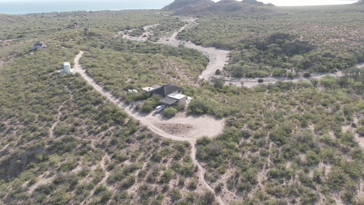 Aerial view of a dirt road and scrubby terrain with small structures near the bottom of frame.