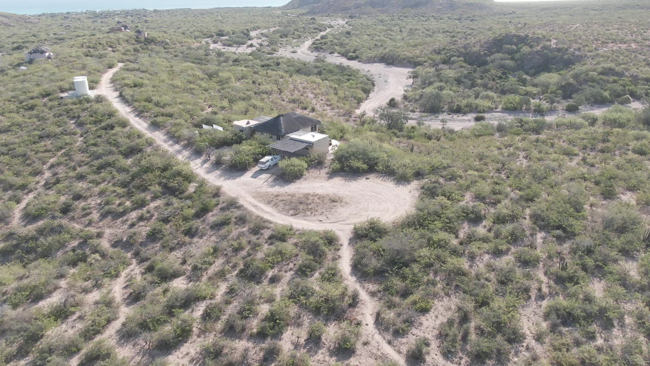 Aerial approach toward a desert house with a white vehicle nearby.