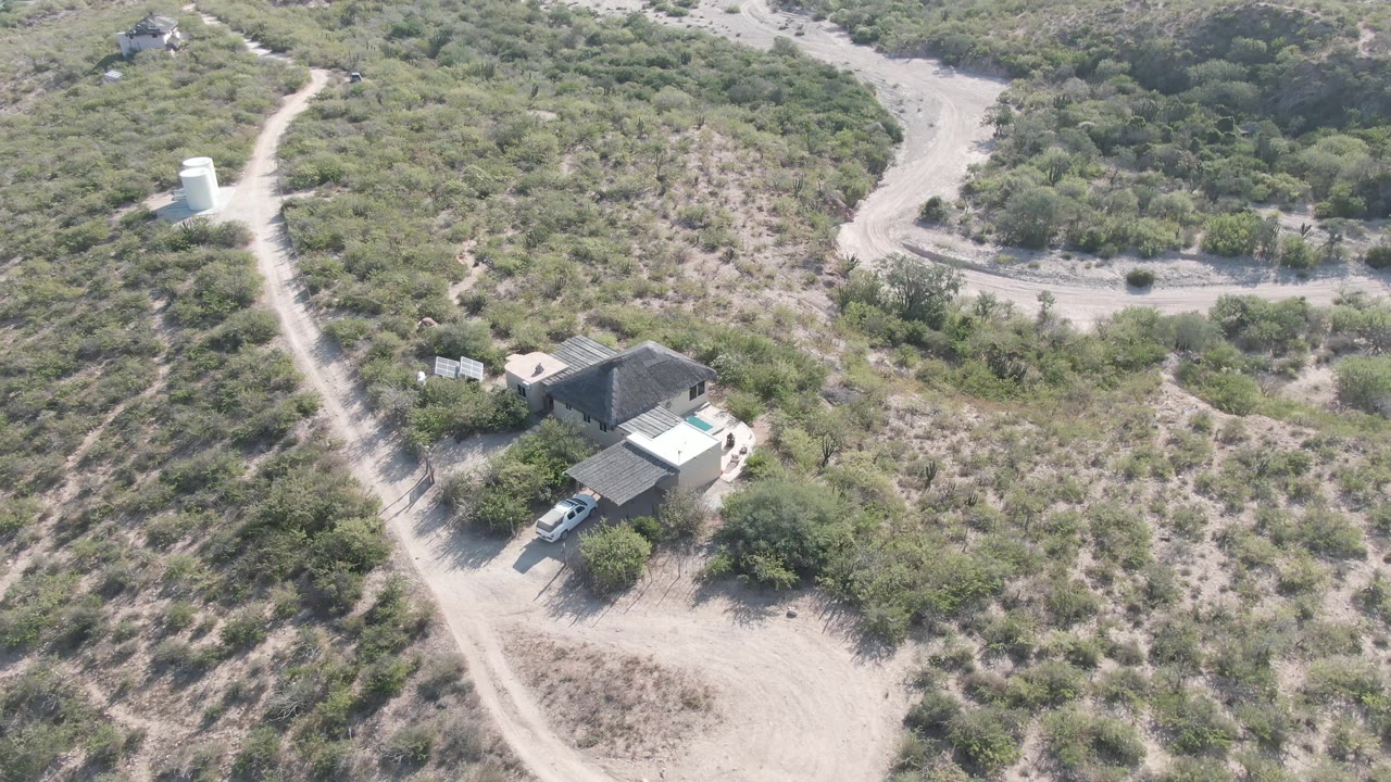 Rural property and winding dirt roads seen from above in scrubby terrain.