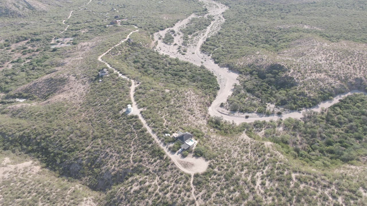 Aerial frame of a pale road running beside a vegetated wash.
