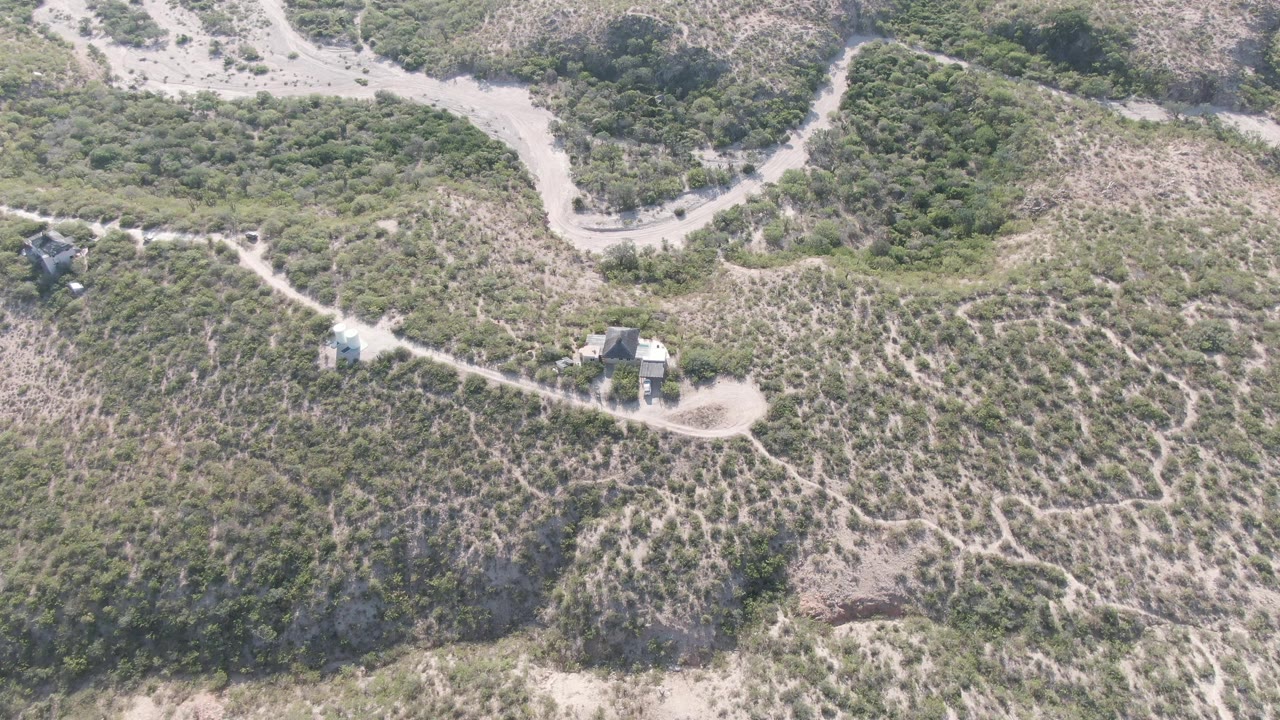 Aerial frame from Cabo Pulmo, Baja California Sur showing a pale dirt road, branching footpaths, scrub-covered hills, small structures, and no visible people at the start of the clip.