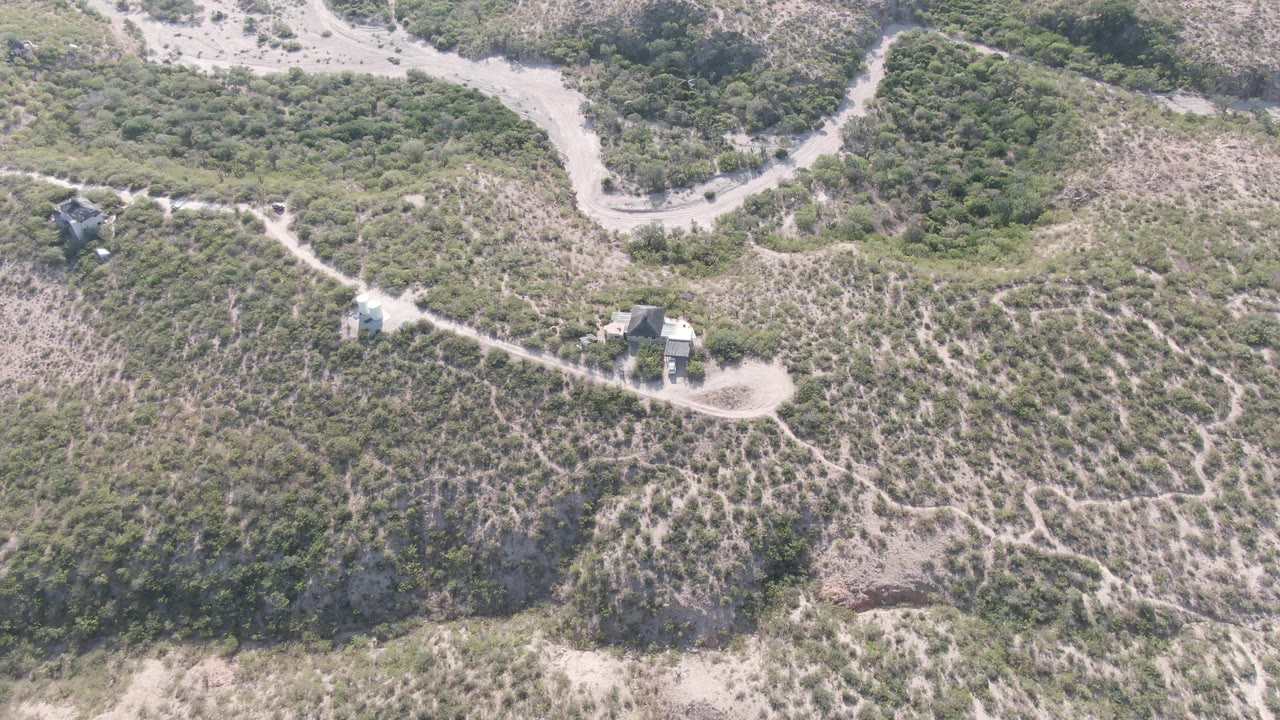 Wide overhead view of a winding dirt road and trails across a dry green hillside.