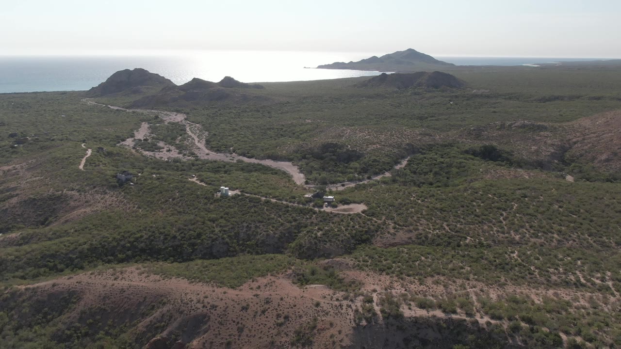 Vehicles travel along a winding dirt road below dark hills near the coast.