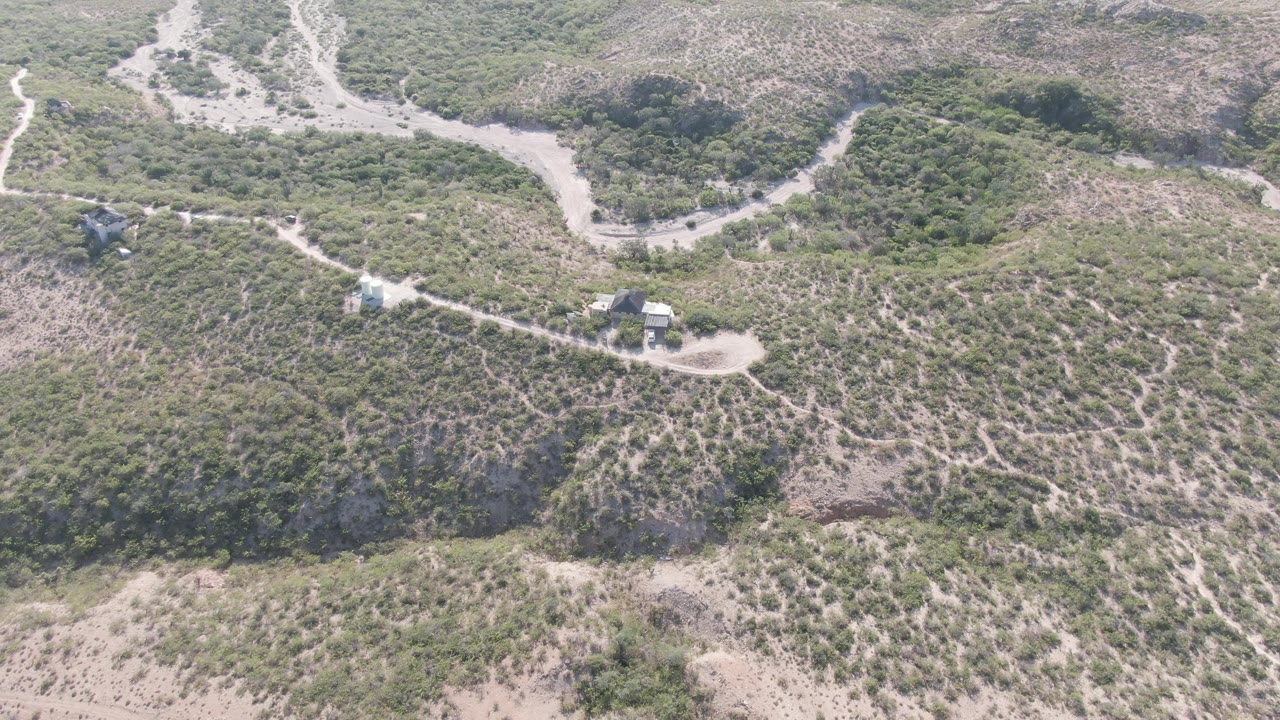 Aerial frame over scrub-covered hills in Cabo Pulmo, Baja California Sur, with pale dirt paths crossing the slope, small structures near the tracks, and no visible people.
