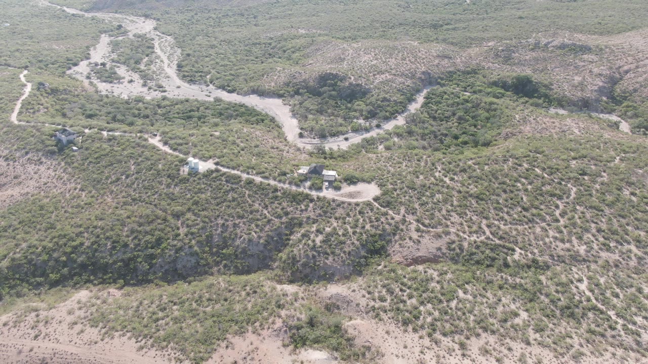Cabo Pulmo aerial still with a winding pale road crossing brushy hills, small structures set along the route, and no visible people in the open terrain.
