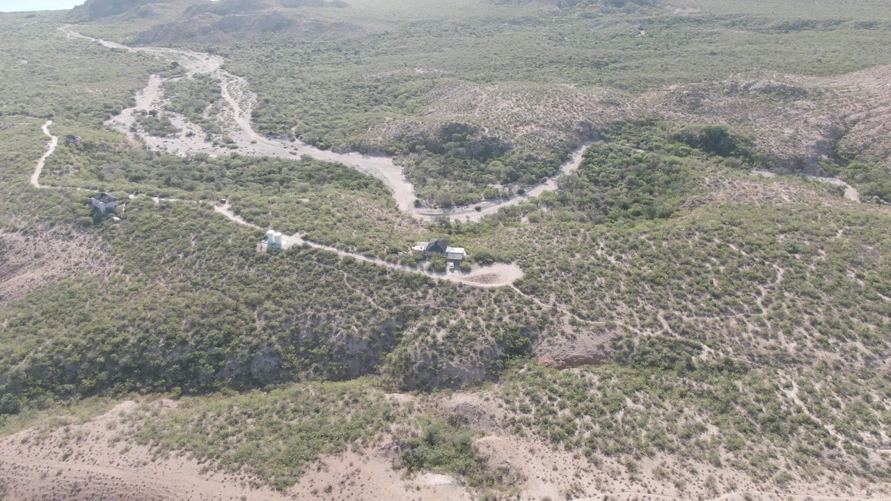 Aerial view of dirt tracks, scrub hills, and distant water at the horizon.