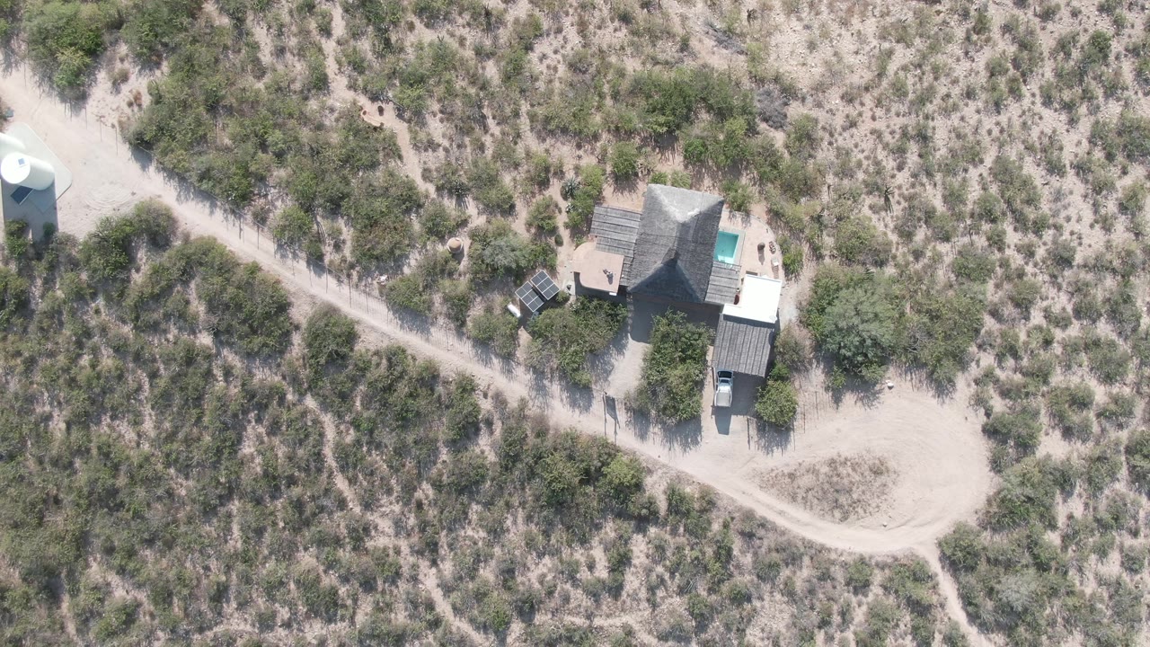 Overhead desert property with dirt road, shrubs, and a small white cylindrical structure nearby.