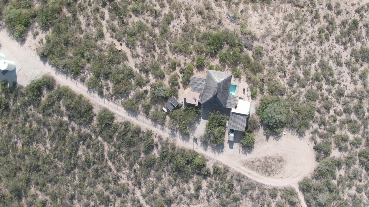 Overhead view in Cabo Pulmo, Baja California Sur showing a sandy desert property with a house, dirt road, sparse shrubs, a small nearby structure, and no visible people.