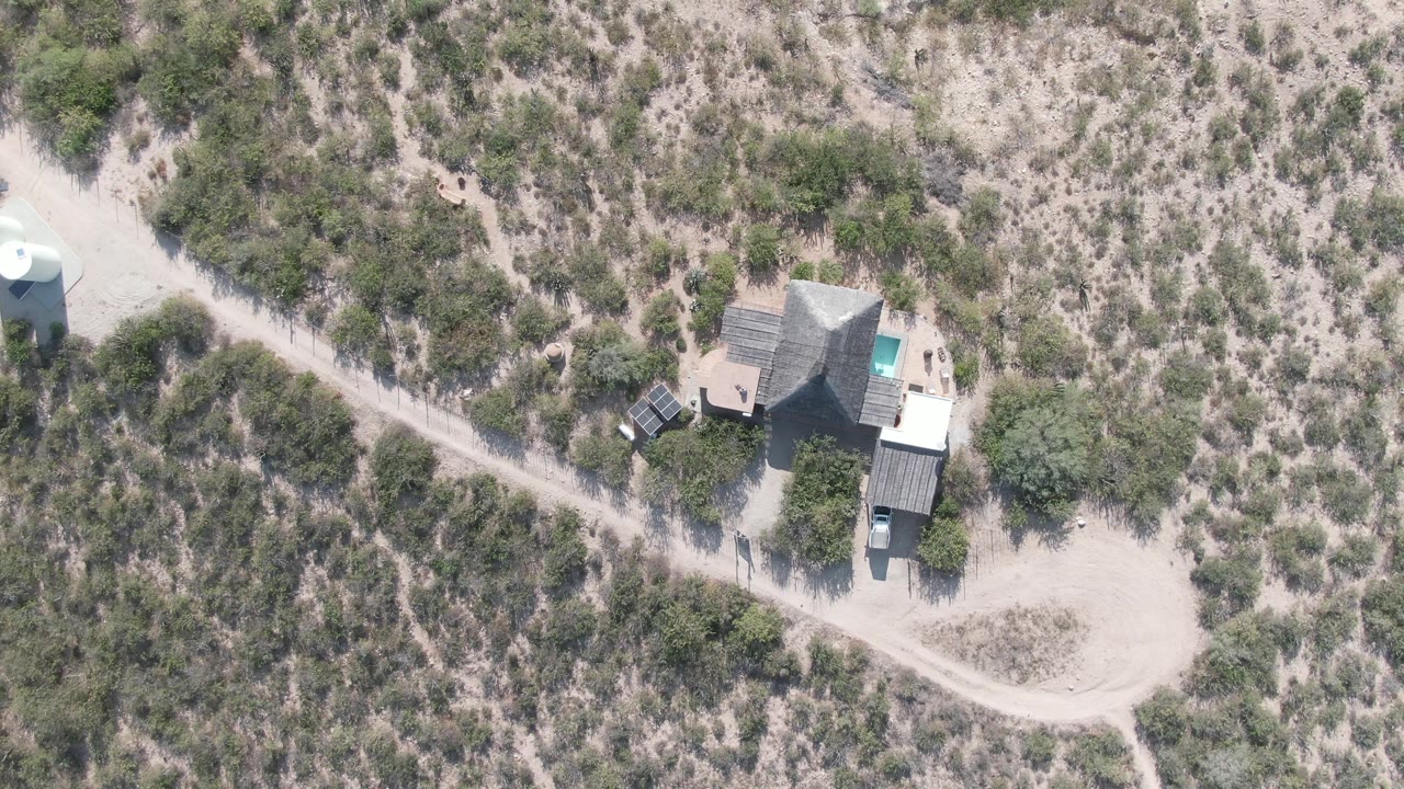 Second overhead frame in Cabo Pulmo, Baja California Sur showing the desert house beside a pale dirt road after the small nearby structure is no longer visible, with no visible people.