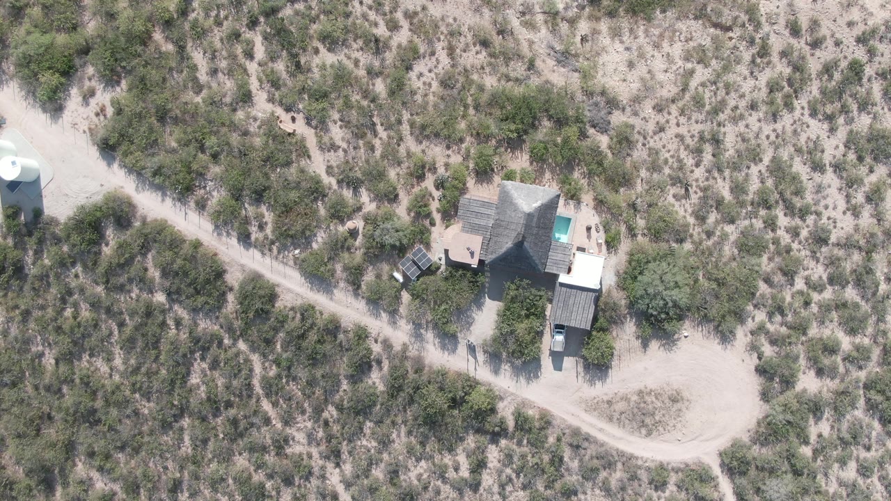 Third overhead frame in Cabo Pulmo, Baja California Sur showing the same sandy lot, house, dirt track, scrub vegetation, and no visible people under hard light.