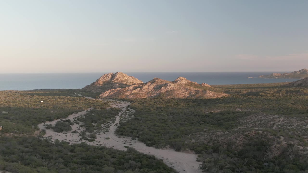 Dirt path through green coastal hills with ocean beyond rocky mountains.