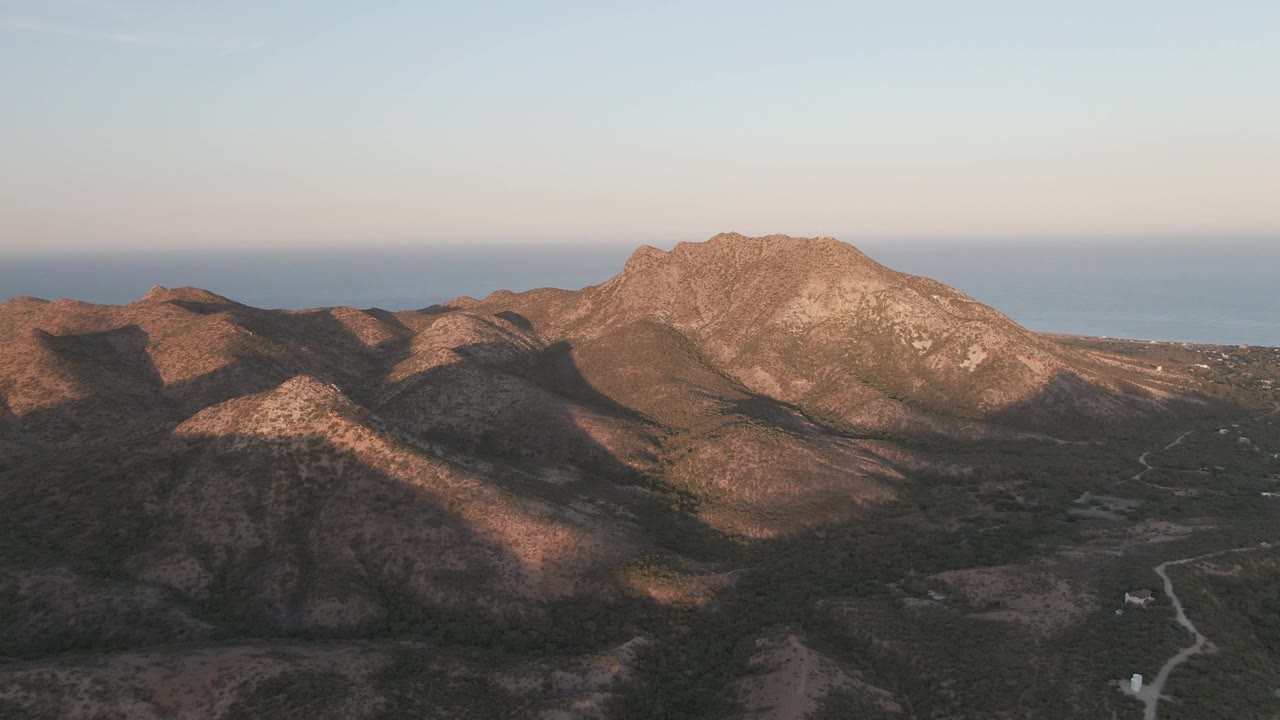 Cabo Pulmo, Baja California Sur aerial view with rocky ridges in warm side light, sparse vegetation below, the sea on the horizon, and no visible people.