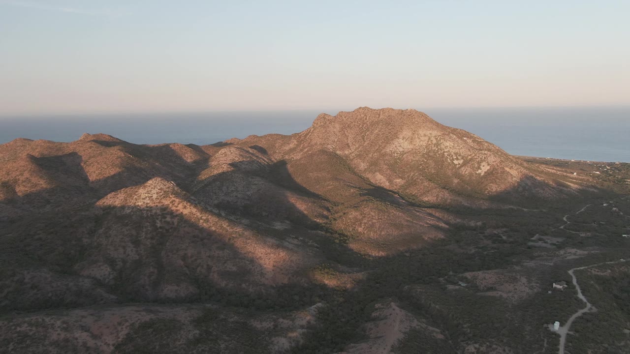 Rocky ridges and shadowed valley with a dirt road and sea beyond.