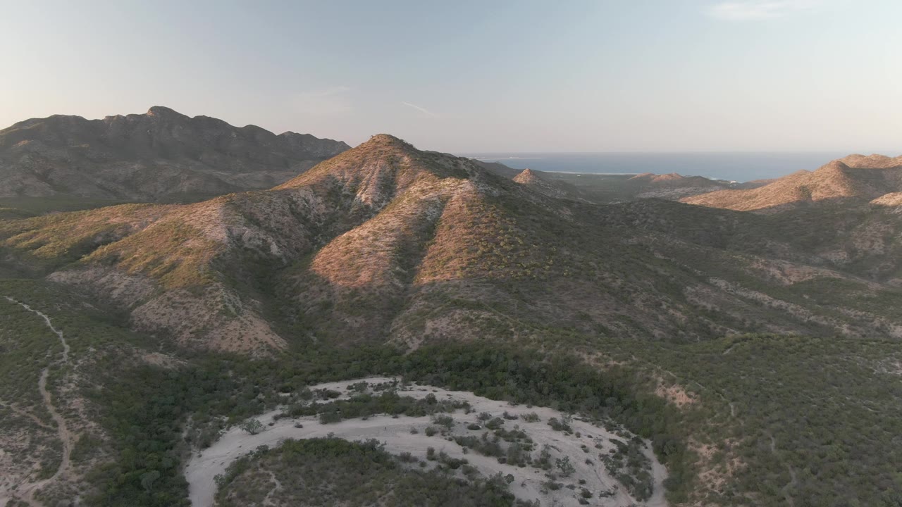 Aerial view of dry mountain ridges and a winding pale road through a valley.