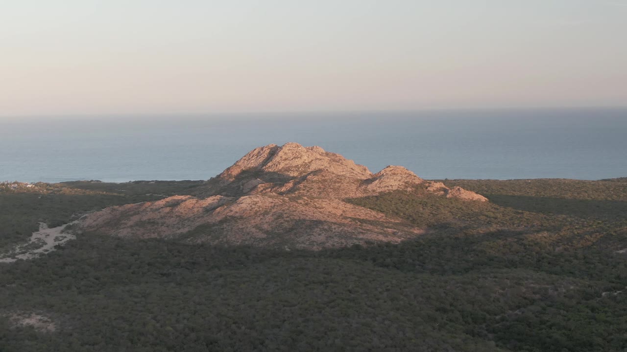 Rocky hill above dense forest with ocean horizon behind it.