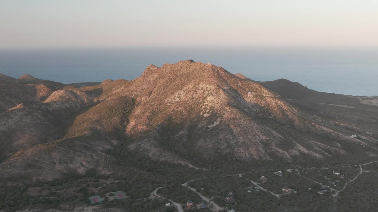 Sunlit mountain ridge above winding dirt roads and distant ocean