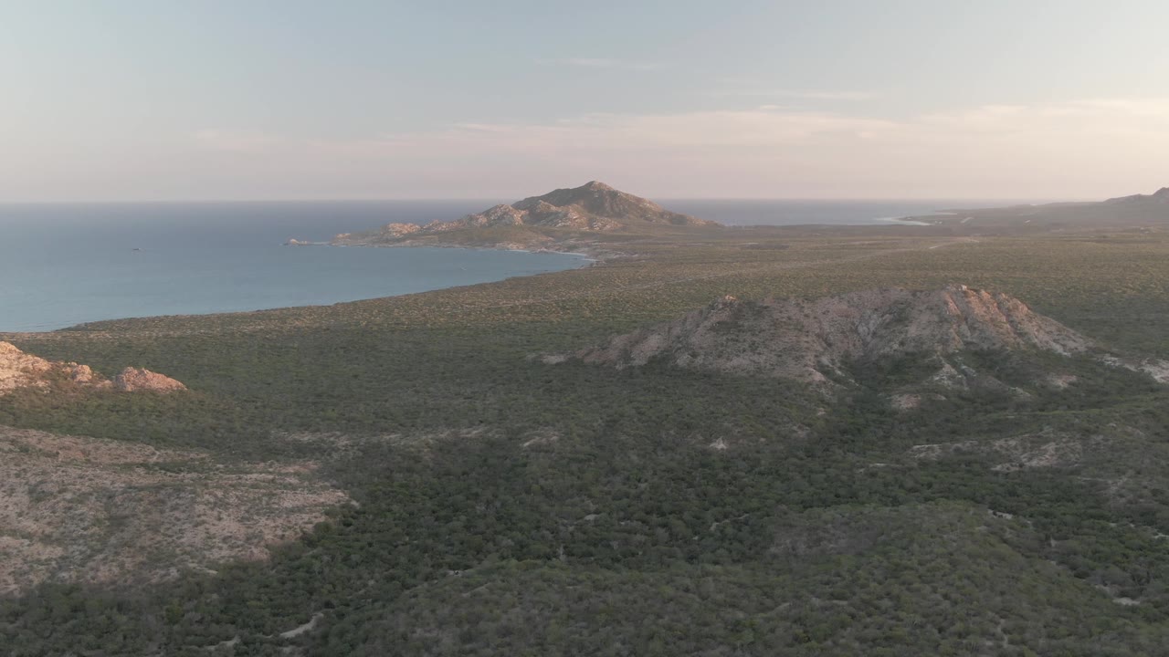 Aerial view of rocky coastal hills, green vegetation, and ocean at dusk.