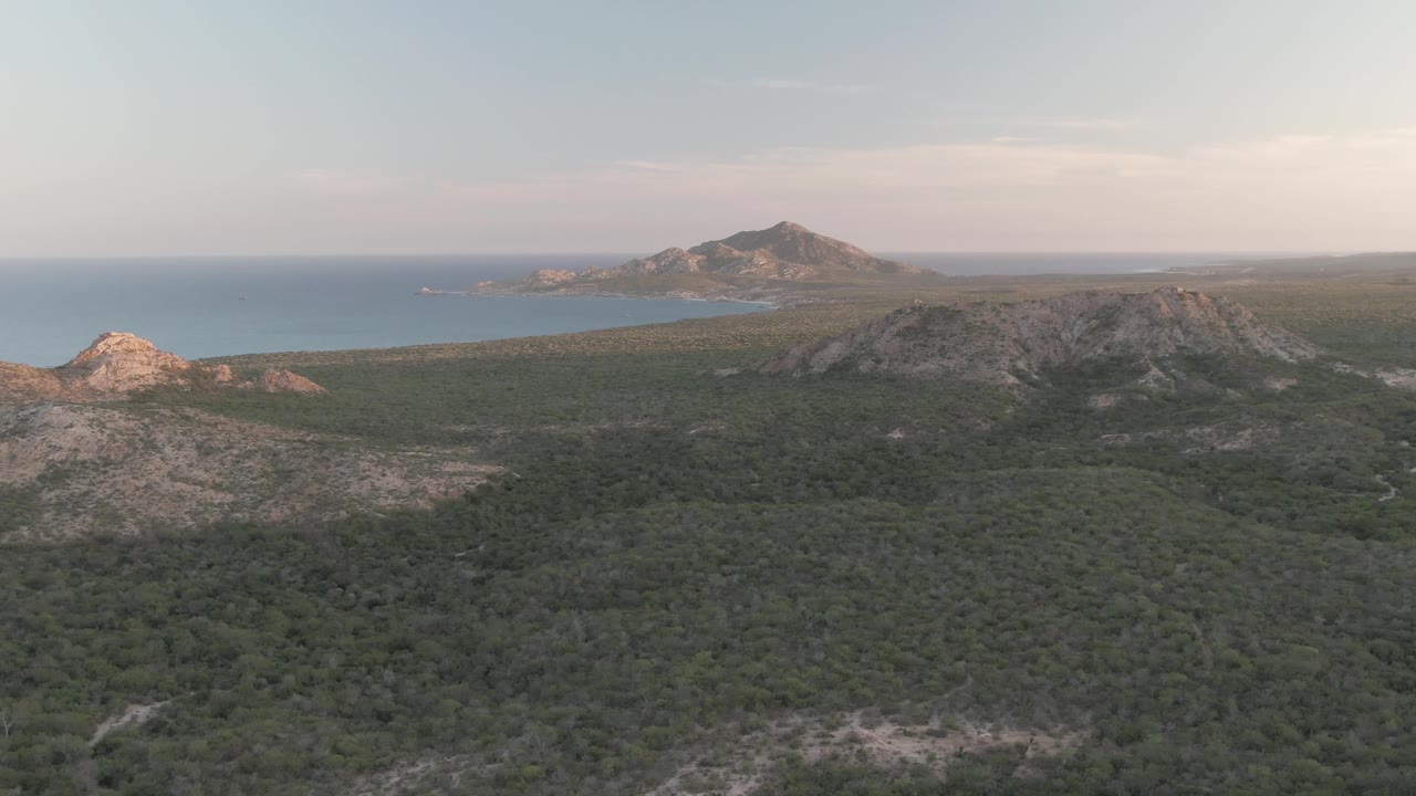 Aerial view of green coastal hills, rocky ridges, and ocean horizon.