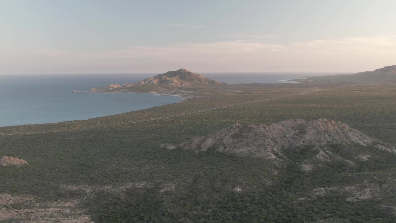 High aerial view of rocky green hills, coastline, ocean, and distant horizon.