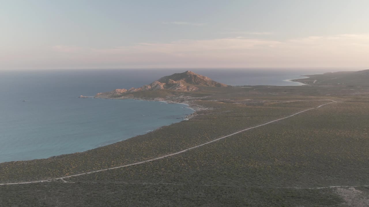 Cabo Pulmo aerial view with the shoreline set farther left, a pale road running through the foreground terrain, low rocky hills in the background, and no visible people.