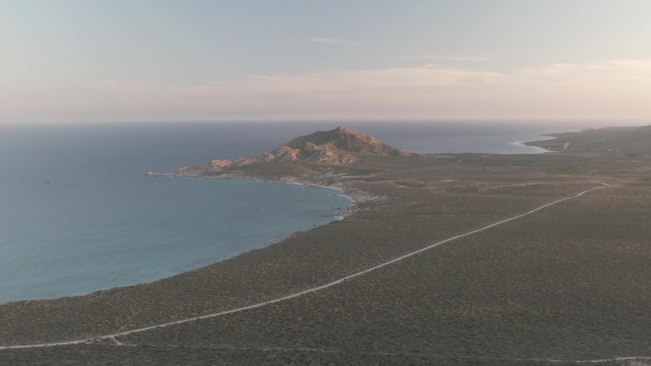 Aerial view of coastal road, ocean, beach, and rocky hill.