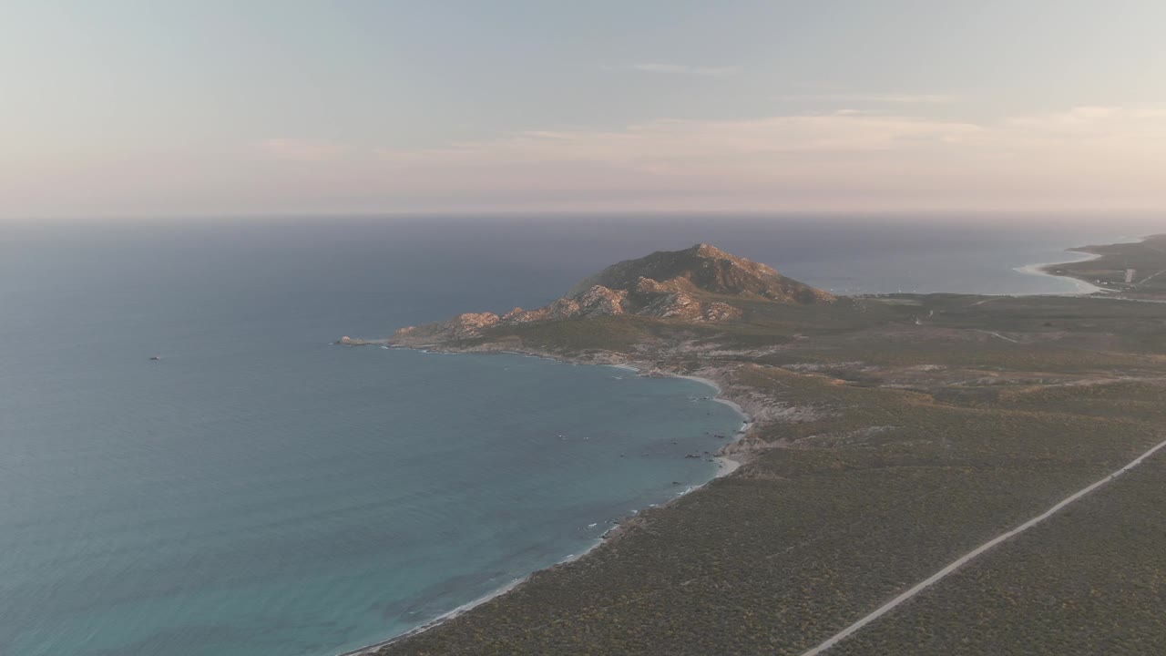 Third frame from the aerial clip shows the Cabo Pulmo coastline with open blue water, a pale surf edge, wide dry land, a diagonal road, distant hills, and no visible people.