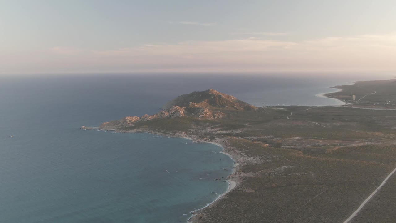 Aerial view of blue ocean, rocky coast, low hills, and a small boat offshore.