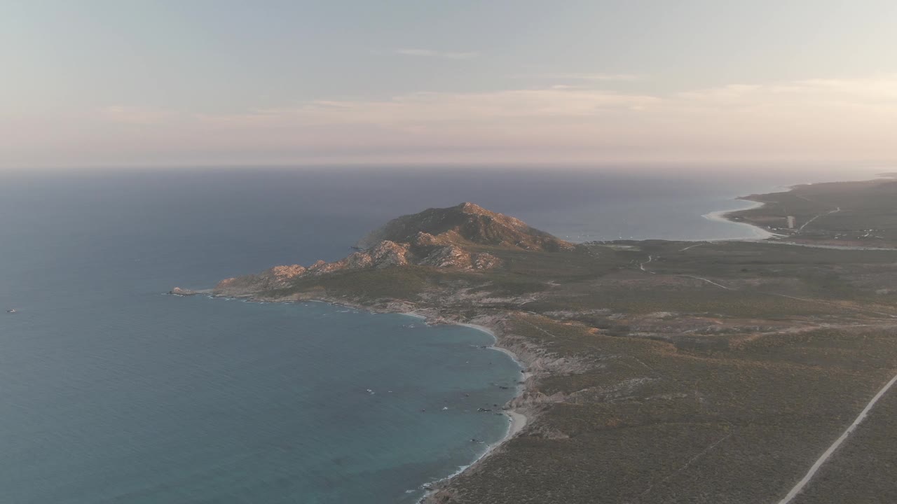 Cabo Pulmo aerial view with calm blue water around the rocky bay, a small boat near shore, brown-green terrain, distant coastline, and no visible people.