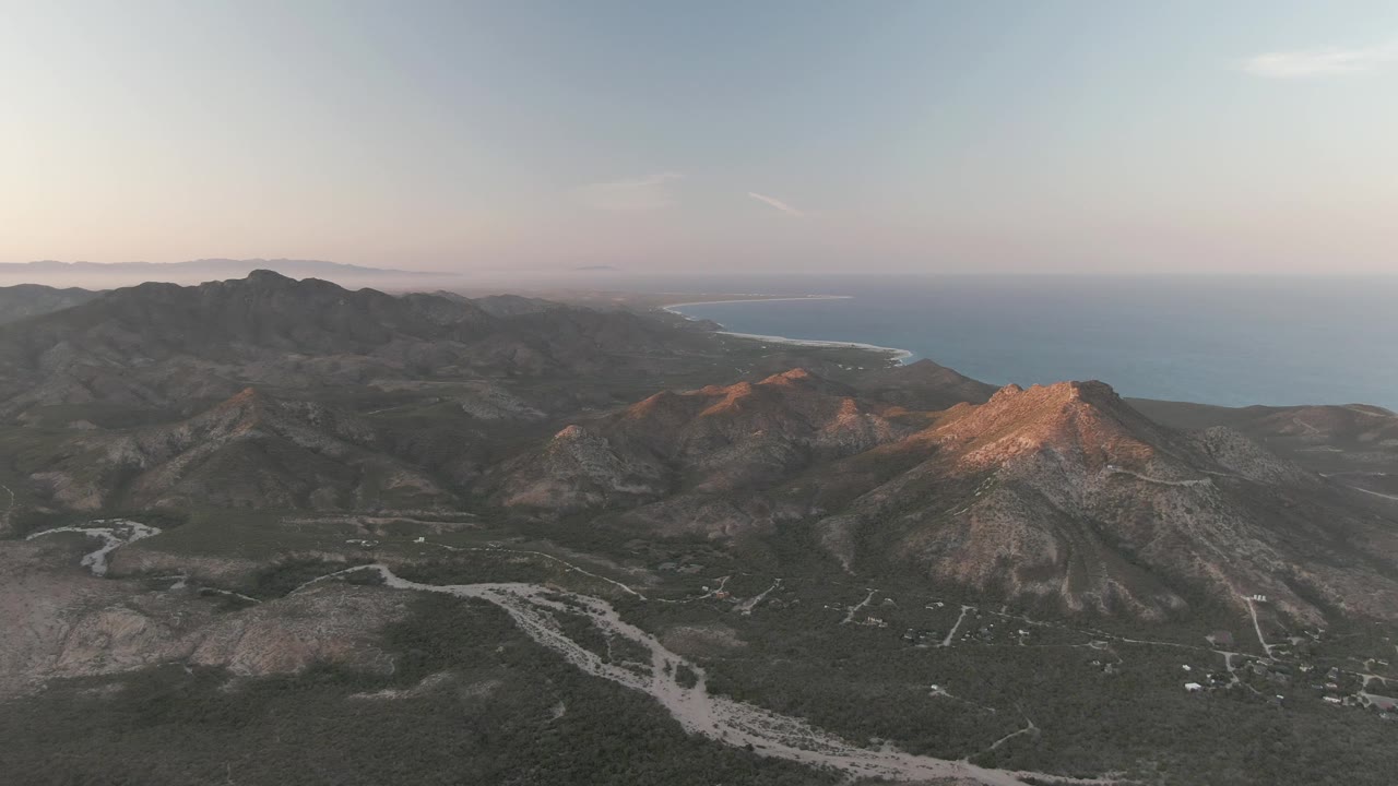 Aerial view of coastal mountains, dry valleys, roads, and distant ocean