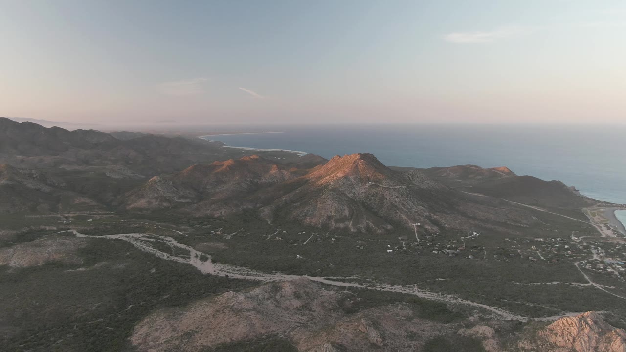 Coastal mountain ridge with road cuts across a scrubby valley and ocean beyond.