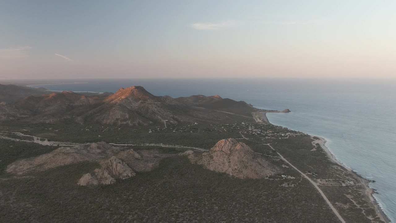Cabo Pulmo aerial frame with the main rocky peak left of center, the ocean on the right, a pale road below, and no visible people in the landscape.