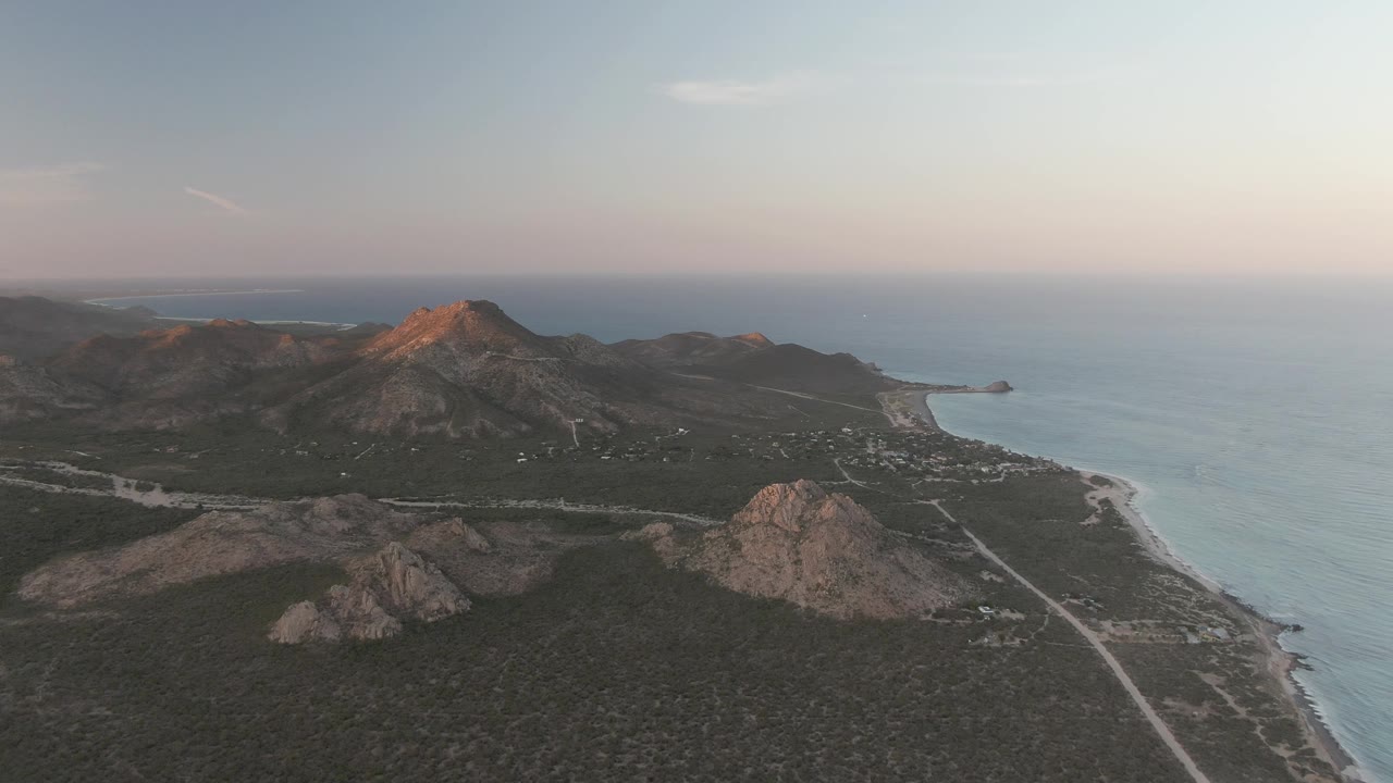 Drone-like view of a coastal road below rocky mountains and ocean water.