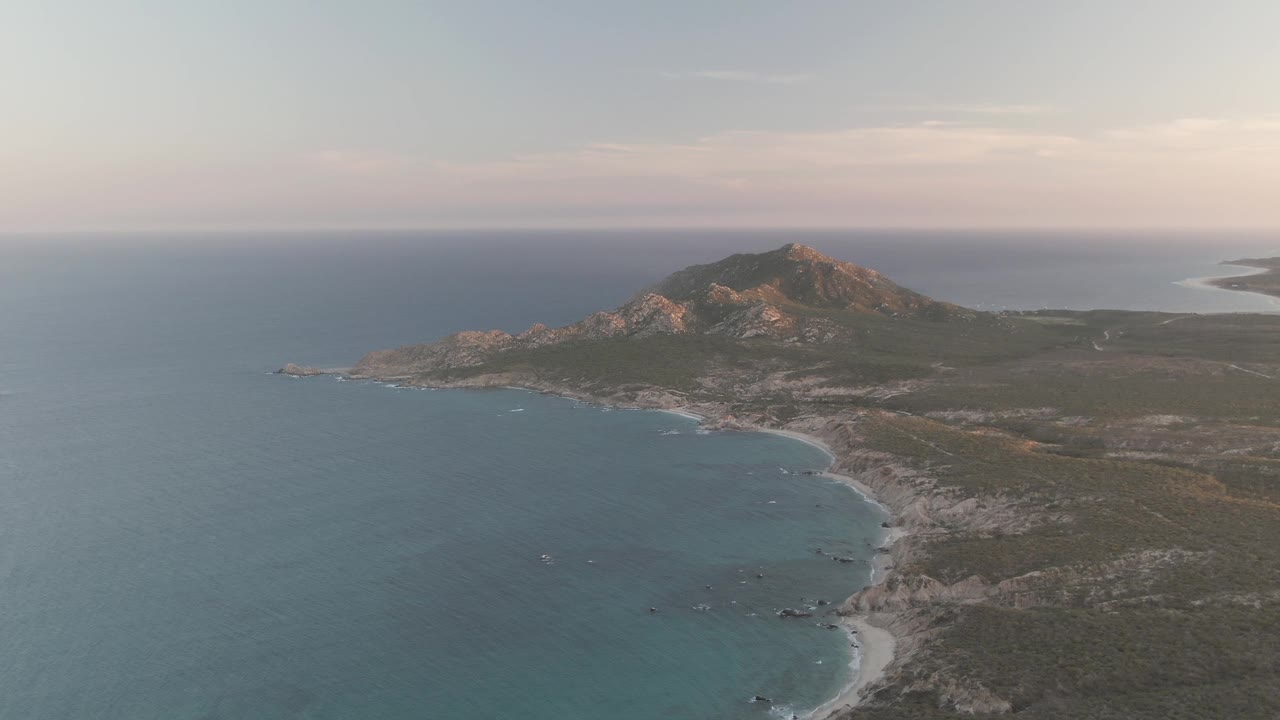 Aerial view of ocean, beach, scrubland, and a coastal mountain.