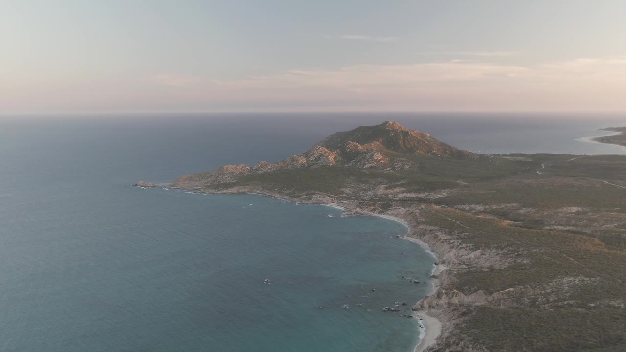 Dusk aerial view of Cabo Pulmo coast with ocean foreground and mountain beyond.