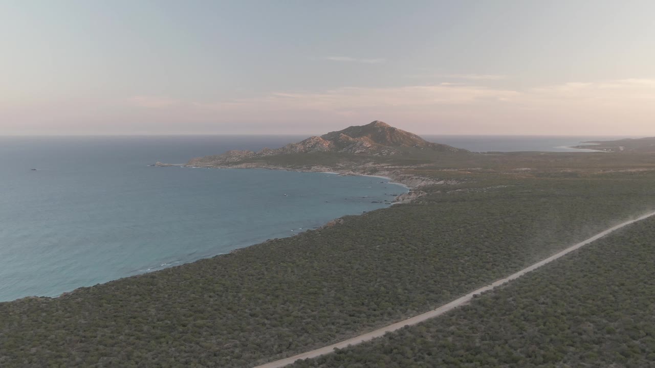 Aerial coastline with scrubland foreground, ocean, road, and hill at soft light