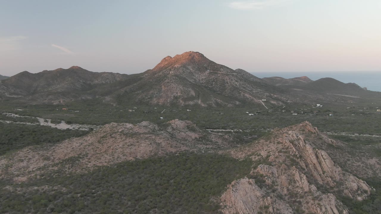 Wide aerial view of a mountain peak beyond rocky desert hills.