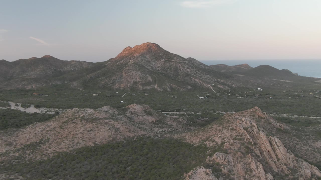 At two seconds, the Cabo Pulmo view shows layered ridges in the foreground, the valley road crossing green terrain, a softly lit peak, ocean horizon, and no visible people.