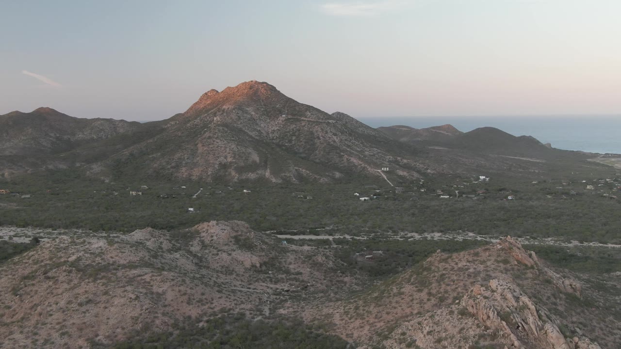 Opening frame of Cabo Pulmo, Baja California Sur, showing foreground rocky hills, a green valley, distant water, and a warm-lit mountain peak with no visible people.