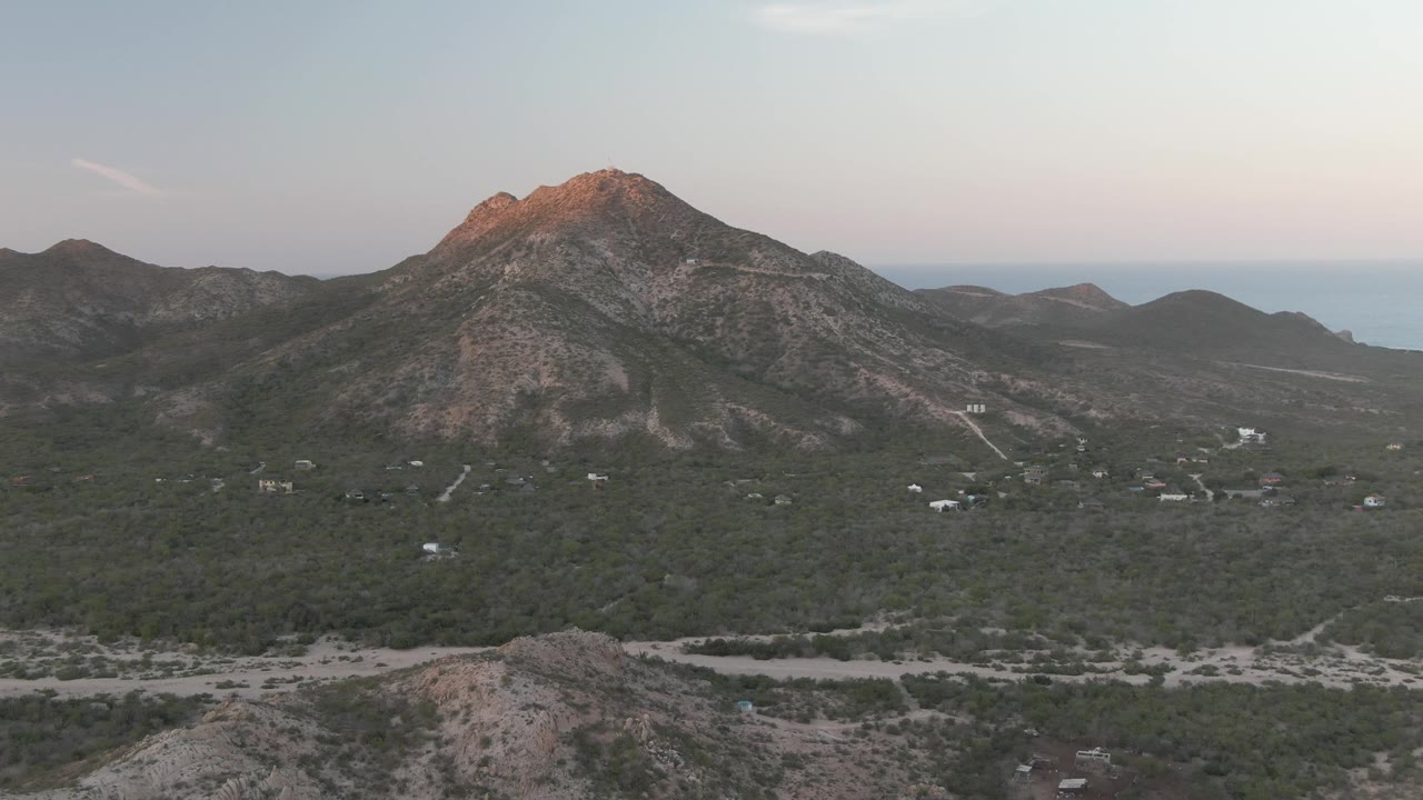 Descending aerial view toward a rocky foreground ridge and mountain valley.
