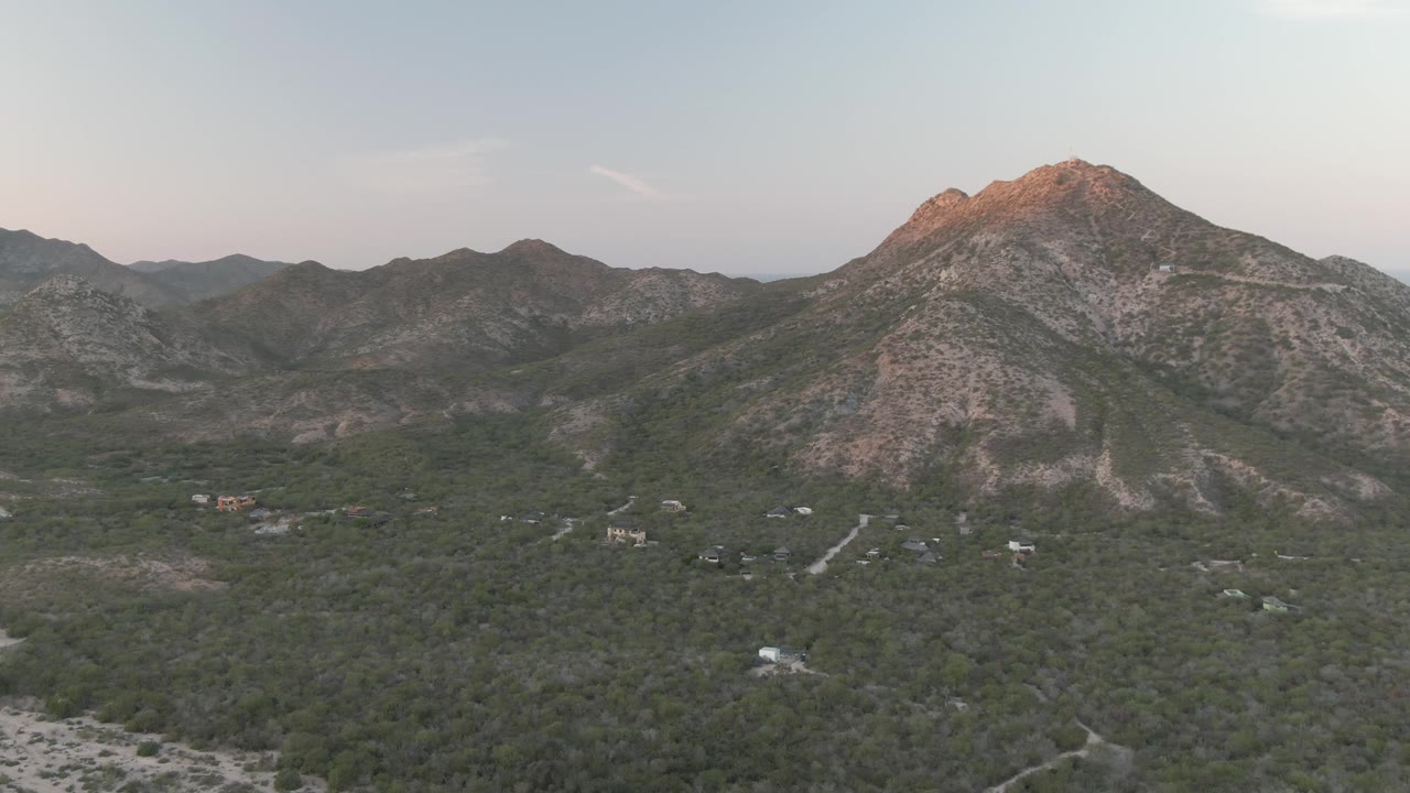 Cabo Pulmo aerial landscape showing a rocky peak near the right side of frame, green brush across the valley floor, small roads and structures, and no visible people.