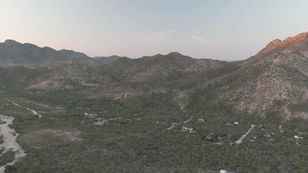 Drone view across a green mountain valley with dirt roads.