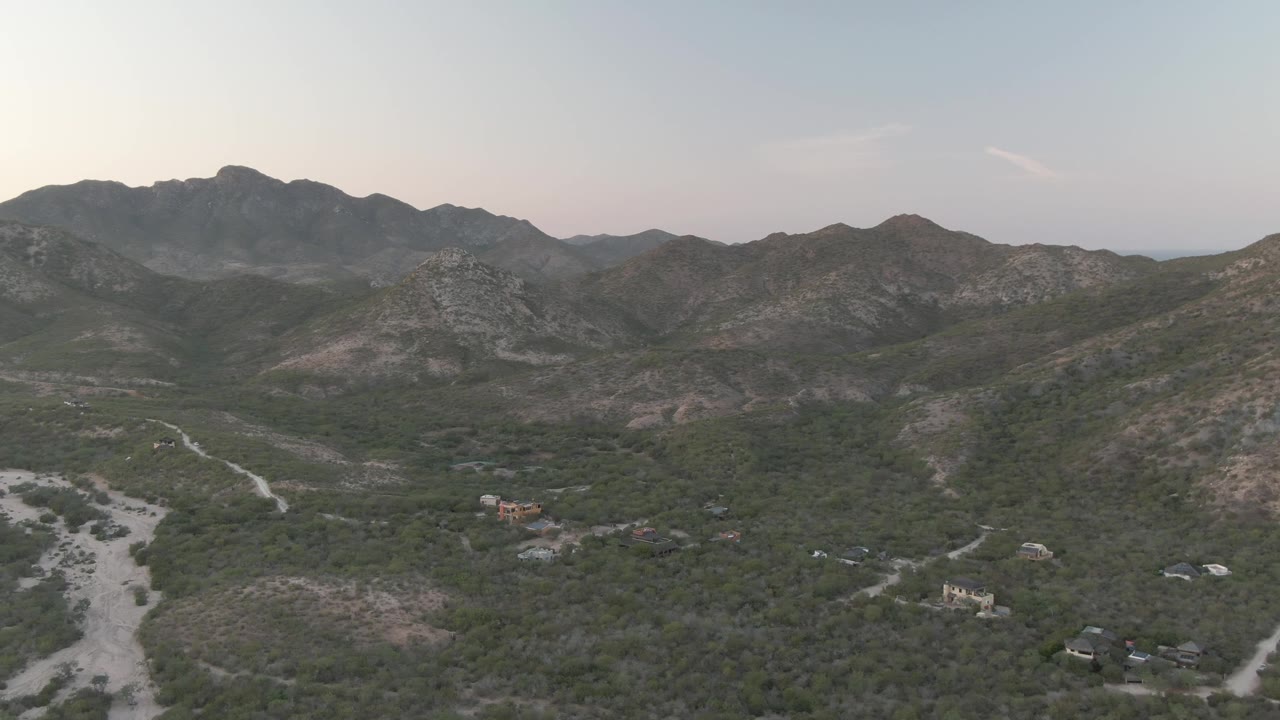 Rocky mountain range above a scrub valley with roads and small buildings under soft light.