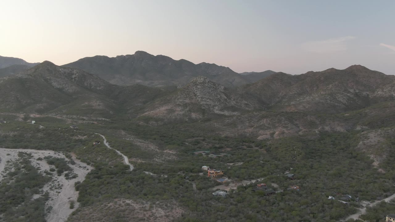 Wide aerial valley view with dry wash, scattered trees, and distant ridges