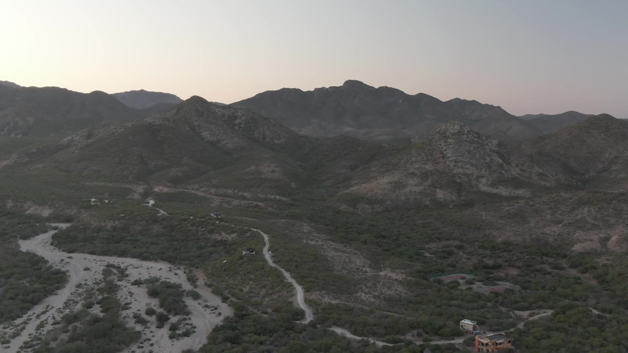 Aerial valley view with dry riverbed in the foreground and mountains under soft light.