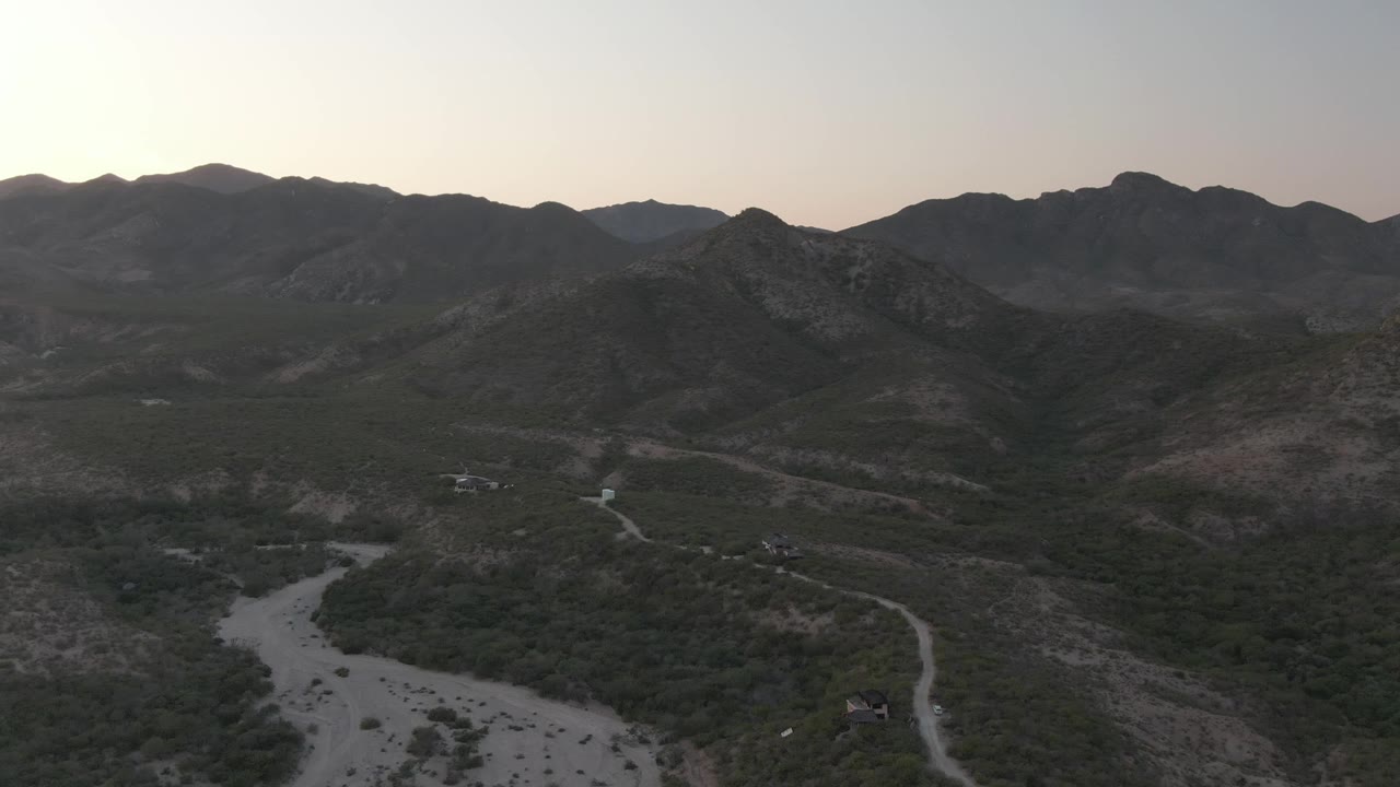 Elevated view of winding dirt roads crossing a dark mountain valley with a dry wash below.