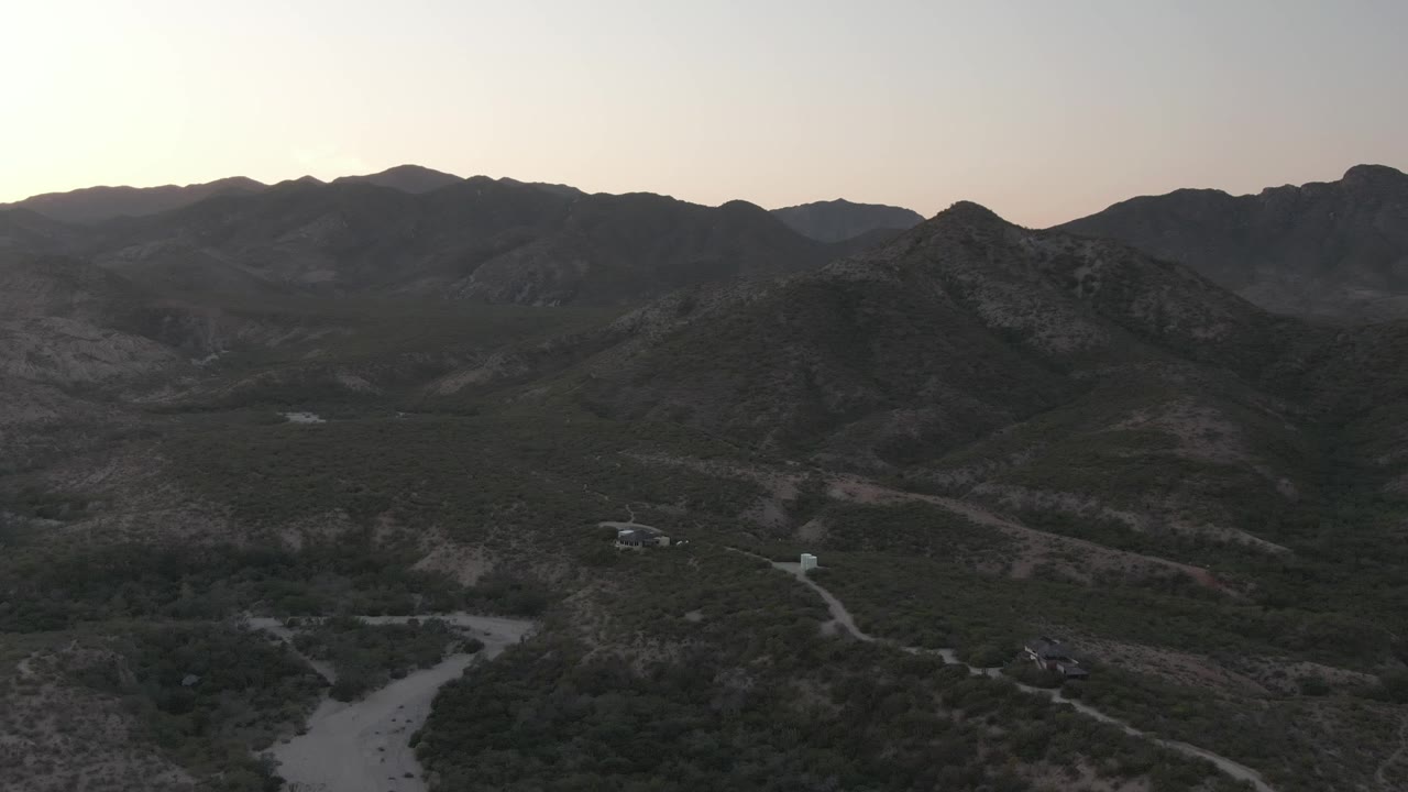 A small vehicle appears on the winding dirt road in Cabo Pulmo, Baja California Sur, with rocky hills and scrub vegetation around it and no visible people.