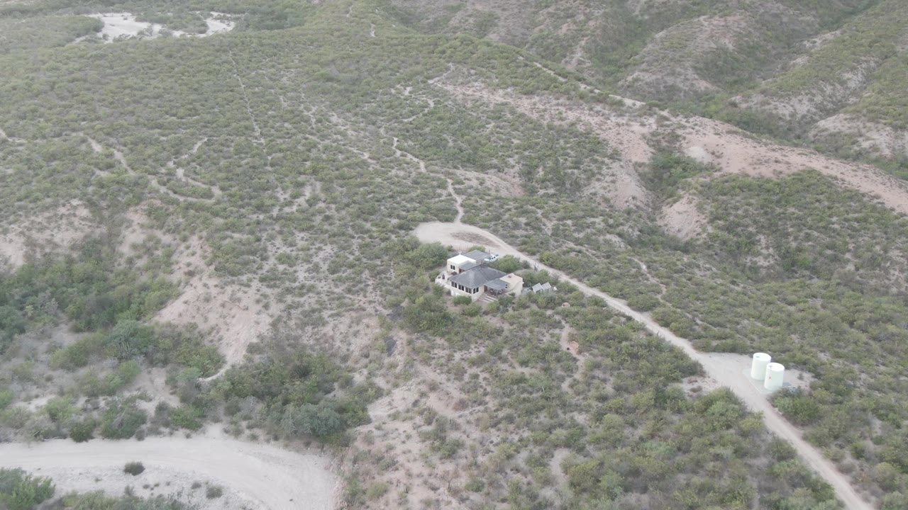 Drone perspective over Cabo Pulmo, Baja California Sur showing the dirt road running from the lower right toward a small house, with white water tanks nearby and no visible people.