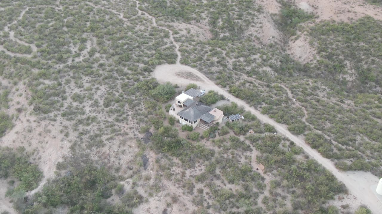 Aerial desert road leading past a house and tanks