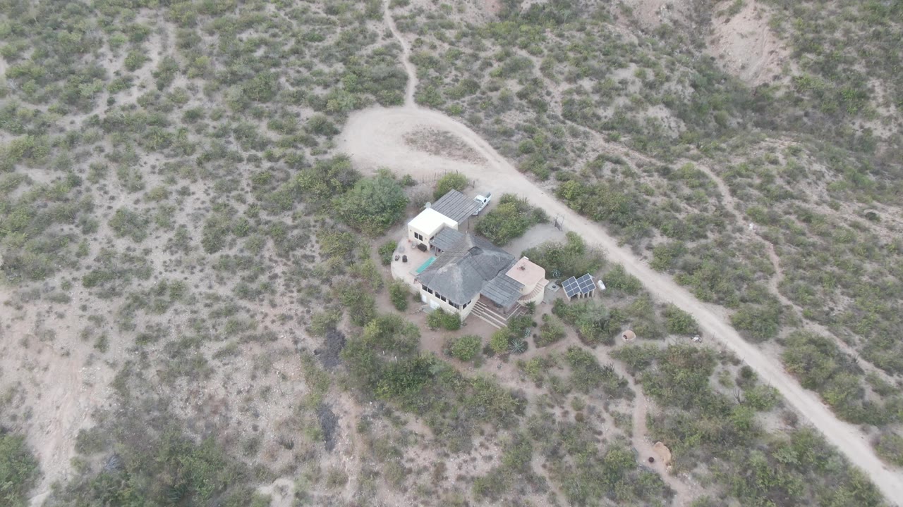 Aerial view in Cabo Pulmo, Baja California Sur showing a desert house, solar panels, a pale dirt road, scattered shrubs, and no visible people.